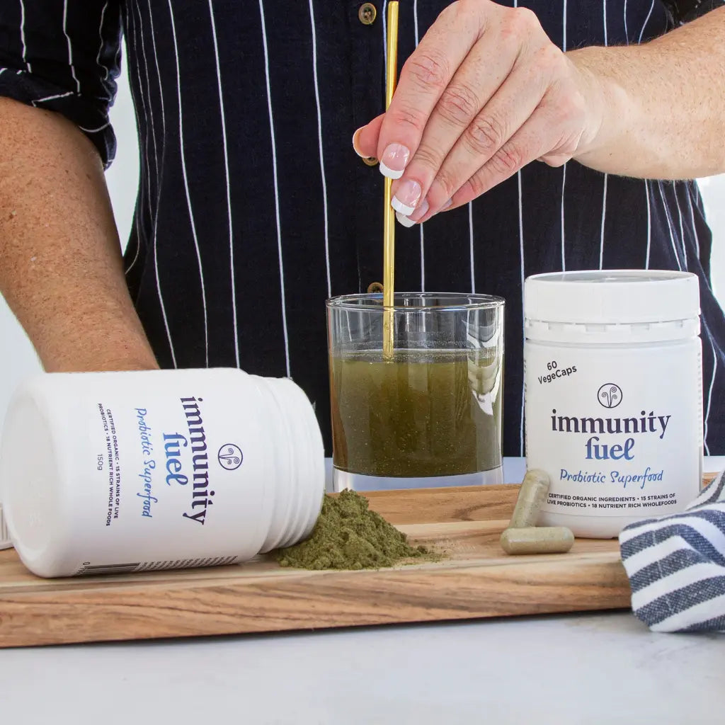 Immunity Fuel certified organic powder and capsules tubs on wooden tray and powder being mixed in glass of water