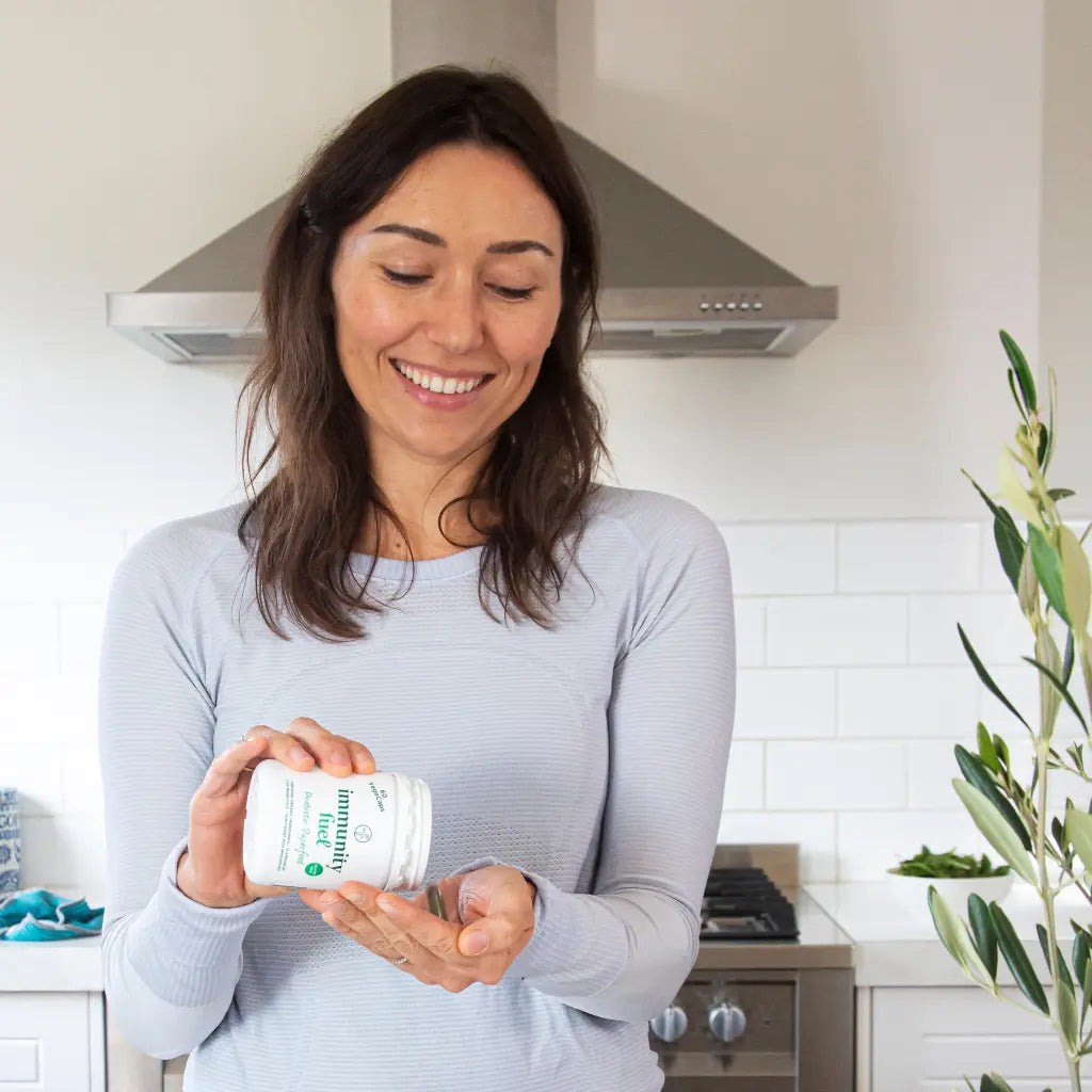 Woman holding an immunity fuel probiotic capsules supplement bottle in a kitchen