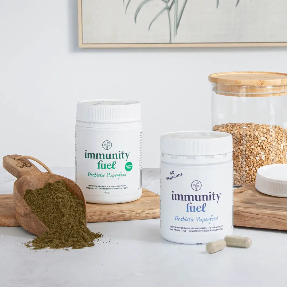 Two containers of 'immunity fuel' on a white surface with a wooden scoop of powder and a glass jar in the background.
